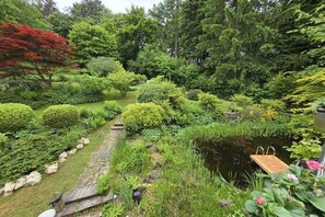 Ein üppiger Garten mit Teich, einem Steinweg und einer Holzterrasse.
