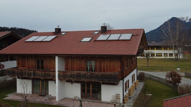 Ein zweistöckiges Gebäude mit rotem Ziegeldach, Holzbalkonen und einem kleinen Garten.