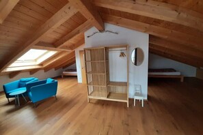 A loft bedroom with a sloped ceiling, wooden beams, a skylight, a bed, a wardrobe, a small table, and a blue sofa.