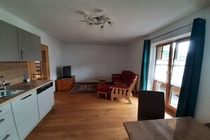 Een ruimtelijke woonkamer met kitchenette, een eethoek en een zithoek met uitzicht door een glazen deur.
