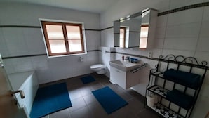 Ein Badezimmer mit Toilette, Waschbecken, Spiegel, Fenster und einem Ablagebereich mit Handtüchern.