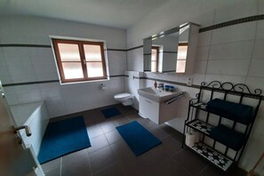 A bathroom with a toilet, sink, mirror, window, and a shelf with towels. - Holiday apartment with 2 bedrooms (Mittenwald)