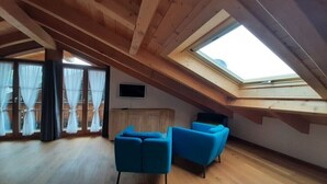 Ein Zimmer mit schrägen Wänden, Holzbalken, einem Oberlicht, einem Holzschrank und zwei blauen Stühlen.