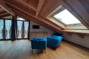 A room with a sloped ceiling, wooden beams, a skylight, a wooden cabinet, and two blue chairs. - Holiday apartment with 2 bedrooms (Mittenwald)