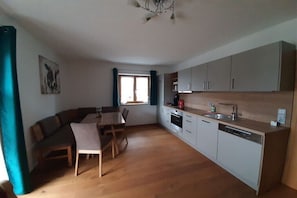 A compact kitchen with a dining area, wooden flooring, and a window with curtains.