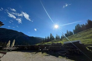 A clear sky with the sun shining, a mountain in the background, and a pile of logs.