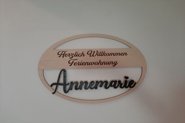 Un panneau circulaire en bois portant l’inscription « Herzlich Willkommen Ferienwohnung Annamarie », qui indique l’entrée d’une location de vacances appelée Annamarie et souhaite la bienvenue aux visiteurs.