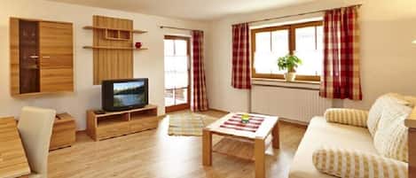 Una sala de estar con televisor, muebles de madera, un sofá y una ventana con cortinas.