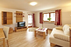 Sala de estar com televisão, móveis de madeira, um sofá e uma janela com cortinas.