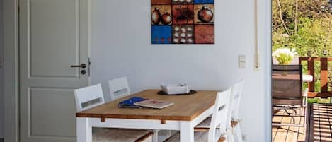A dining area with a wooden table and white chairs, a hanging light fixture, and a door to the left.
