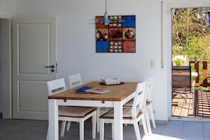 Ein Essbereich mit einem Holztisch, weißen Stühlen, einer hängenden Leuchte und einer Tür links.