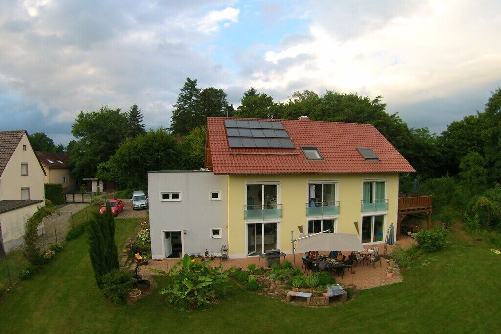 A two-story house with a red-tiled roof, a balcony, and solar panels.