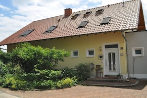 Uma casa de dois andares com telhado de telhas vermelhas, porta da frente e pequena varanda.