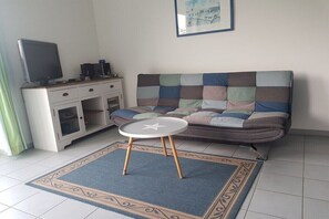 Een woonkamer met een bank, een klein rond tafeltje, een televisie op een kast en een ingelijst kunstwerk aan de muur.