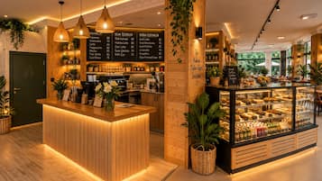 Een café interieur met een houten toonbank, hangende lampen en een vitrine met gebak.