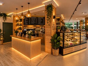A coffee shop interior with a wooden counter, hanging lights, and a display case with pastries. - Antalya Bed & Breakfast (Konyaalti)