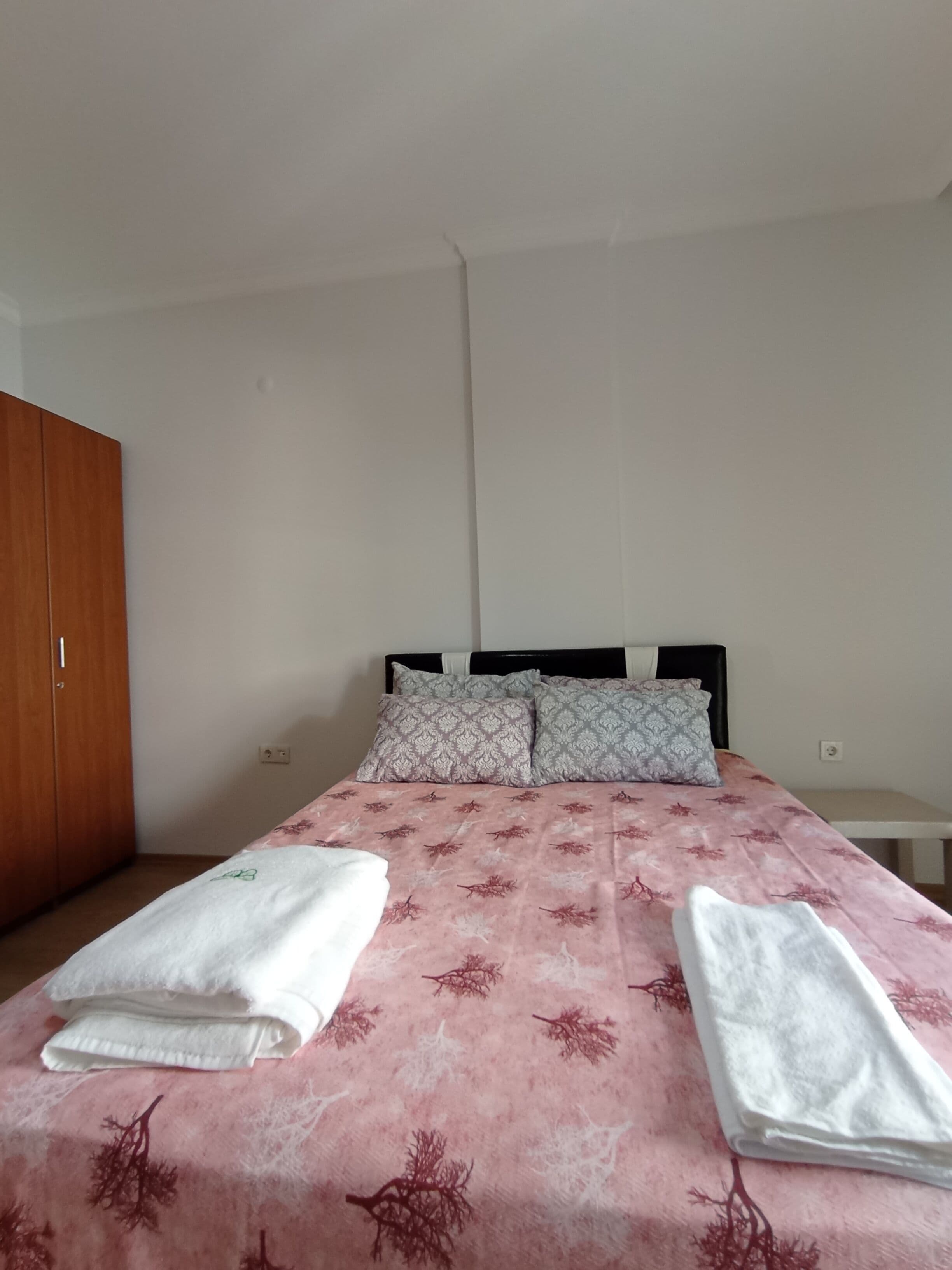 Een eenpersoonsbed met een bloemenbedekking, twee kussens en een houten garderobe.