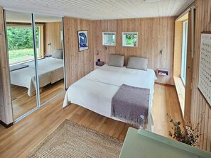Ein Schlafzimmer mit einem großen Bett, einem kleineren Bett, Holzwänden und Blick auf Grünflächen.