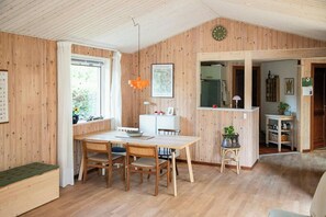 Ein Holzinterieur mit einem Esstisch, Stühlen, einer kleinen Küchenzeile und einer Uhr an der Wand.