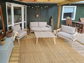 Een overdekt terras met een bank, stoelen en een tafel.