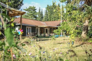 Ein Haus mit überdachter Veranda, einem Garten mit verschiedenen Pflanzen und einem blauen Auto auf der Auffahrt.