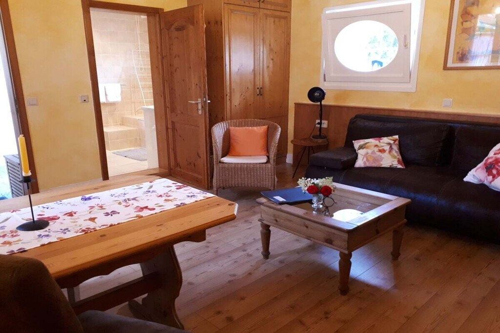 Un soggiorno con un tavolo in legno, un divano, una poltrona in vimini e un piccolo tavolino con un vaso.