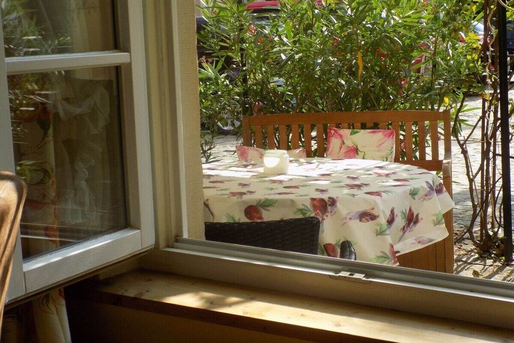 Vista desde la ventana de una mesa con mantel floral, una silla de madera y una vela.