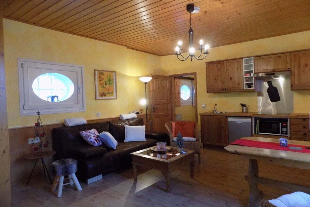 A cozy living room with a sofa, a coffee table, and a dining table. There is a kitchen area with wooden cabinets and a microwave.