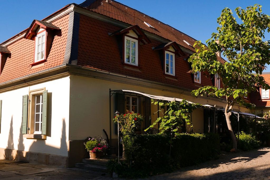 A two-story building with a red-tiled roof, white walls, and green shutters.