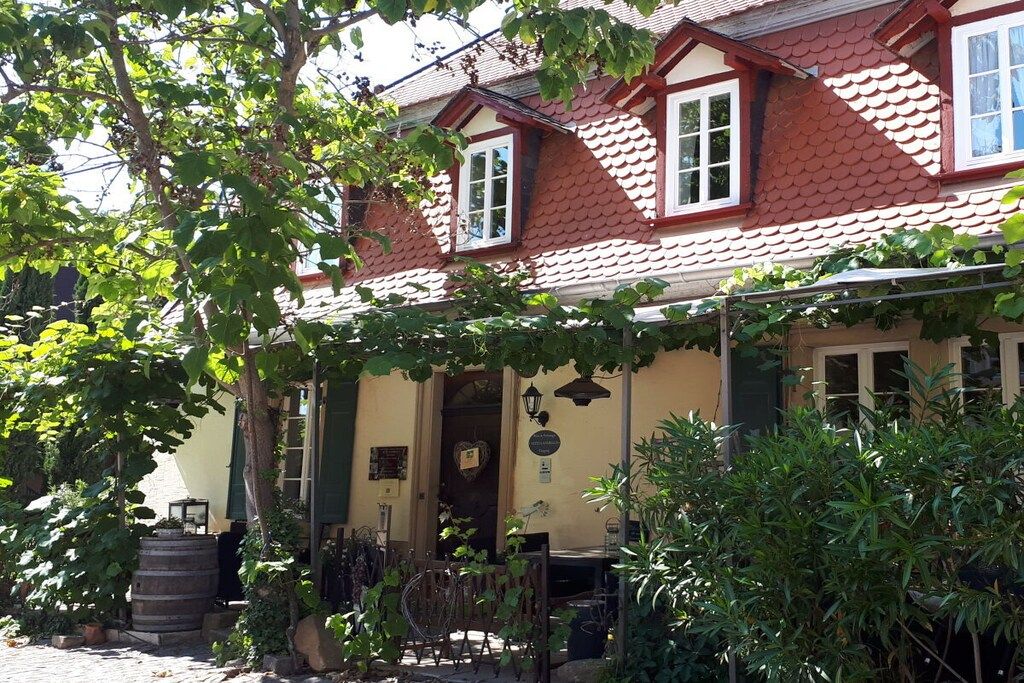 A building with a red-tiled roof, a porch with a bench, and a barrel.