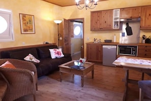 Una sala de estar acogedora con un sofá, una mesa de centro y una mesa de comedor. Hay una zona de cocina con armarios de madera y electrodomésticos modernos.