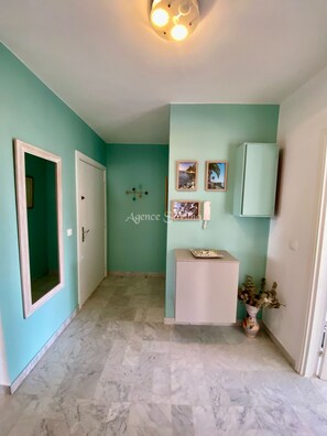 A hallway with teal walls, a white door, a white cabinet, and a ceiling light fixture. - 2-room apartment in a luxury residence—with a pool (Mandelieu-la-Napoule)