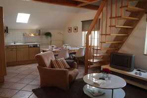 Un salon comprenant un canapé, une table basse et un téléviseur. Un escalier mène à un niveau supérieur.