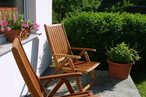 Zwei Holzstühle auf einer Terrasse mit Blumentöpfen.