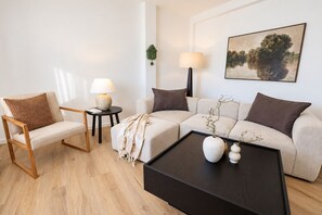 Ein modernes Wohnzimmer mit Sofa, Sessel, Couchtisch und Lampe.