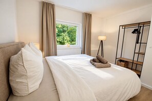Une chambre d’hôtel comprenant un lit, une table de chevet, une lampe, une fenêtre avec des rideaux et une armoire.