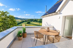 Un balcon avec une table et des chaises, des plantes en pot et une vue sur un paysage verdoyant.