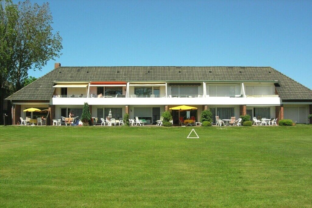 Un bâtiment à deux étages, doté d’un toit plat, d’un espace extérieur aménagé avec des tables et des chaises, et d’une pelouse bien entretenue.