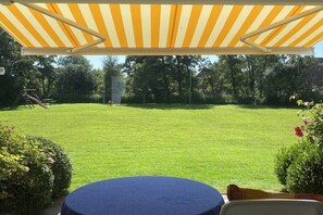 A patio area with a striped awning, a round table, and a lawn in the background. - 4 in the Kiebitzwiese house (Borkum)