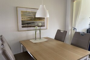 A dining area with a wooden table, two chairs, a white pendant lamp, and a framed painting on the wall. - 4 in the Kiebitzwiese house (Borkum)