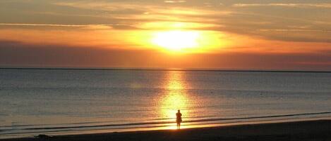 A person standing on a beach during sunset.