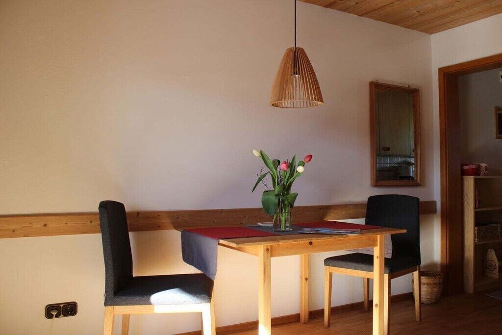 Un'area pranzo con tavolo di legno, due sedie, lampadario e un vaso con fiori.