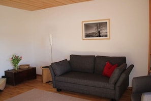 A living room with a grey sofa, a small side table with a vase of flowers, and a framed picture on the wall. - at the Freisl country house (Bad Kohlgrub)
