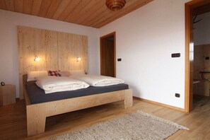 A bedroom with a wooden bed, two wall-mounted lights, a wooden door, and a small bedside table. - at the Freisl country house (Bad Kohlgrub)