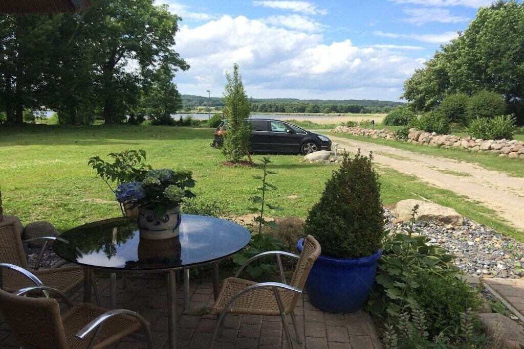An outdoor patio with a table and chairs, surrounded by greenery and a view of the countryside.