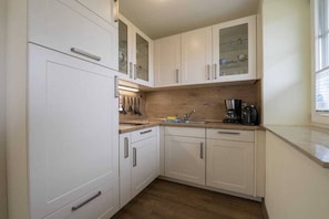 A compact kitchen with white cabinets, a built-in oven, and a coffee maker. - 2 in the country house “Am See” Neuensien (Ostseebad Sellin, OT Neuensien)