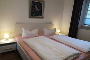 A double bed with white linens, two bedside lamps, a small bedside table with a lamp, and a framed picture on the wall. - 2 in the country house “Am See” Neuensien (Ostseebad Sellin, OT Neuensien)