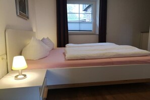 Une chambre à coucher avec un lit, une table de chevet avec une lampe, une fenêtre avec des rideaux et un tableau accroché au mur.