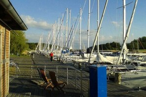 A marina with multiple sailboats docked, a wooden deck, and a brick building on the left. - 2 in the country house “Am See” Neuensien (Ostseebad Sellin, OT Neuensien)