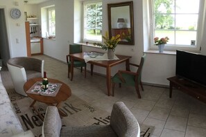 Un salon comprenant un canapé, des fauteuils, une table basse, un téléviseur et un coin repas avec une table et des chaises.